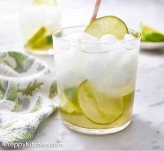 Pinterest graphic of a glass of caipirinha with a linen napkin beside it with another glass and plate of limes in the background.