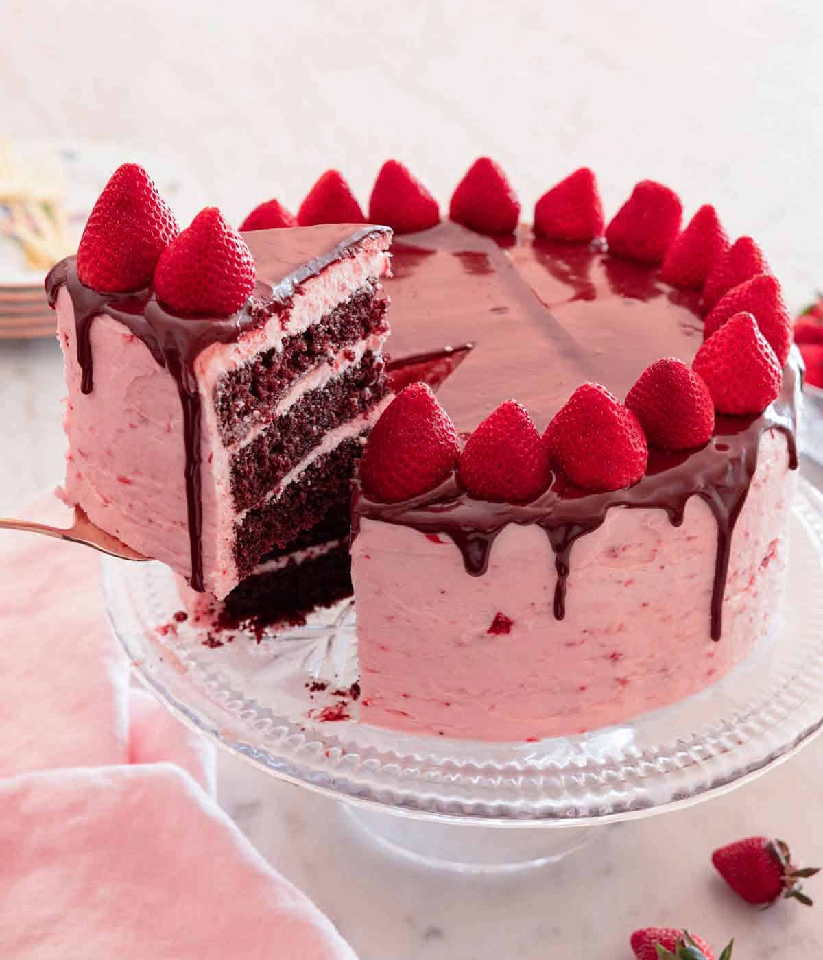 A slice of chocolate strawberry cake lifted from the cake on a clear cake stand.