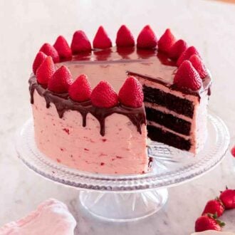 A chocolate strawberry cake with a slice cut out on a cake stand by a bowl of strawberries.