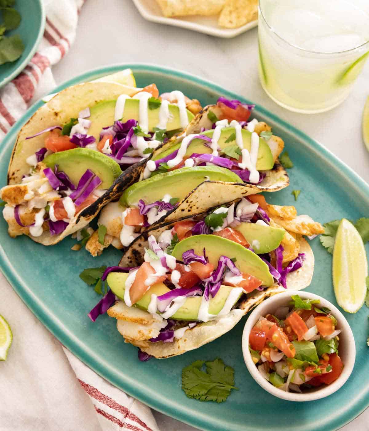 A platter of multiple fish tacos with extra toppings on the side.
