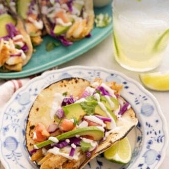 Pinterest graphic of a plate with a fish taco in front of a drink and platter of more tacos.