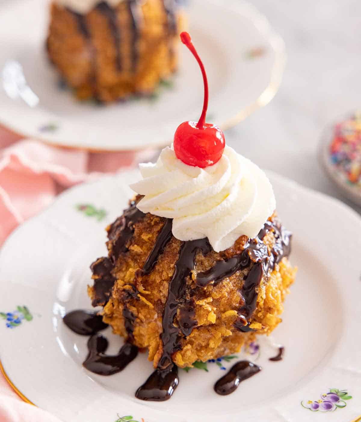 A plate of fried ice cream with chocolate drizzle, whipped cream, and a cherry on top.