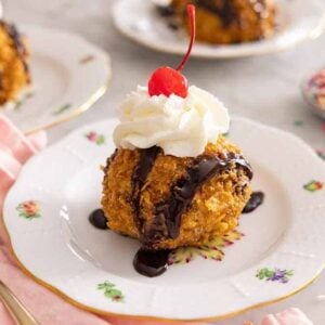 Fried ice cream with whipped cream on top on a plate with another in the background, out of focus.