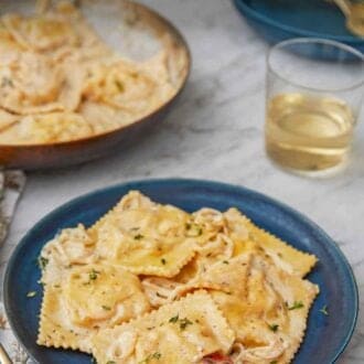 Pinterest graphic of a plate of lobster ravioli by a glass of wine and skillet of pasta.
