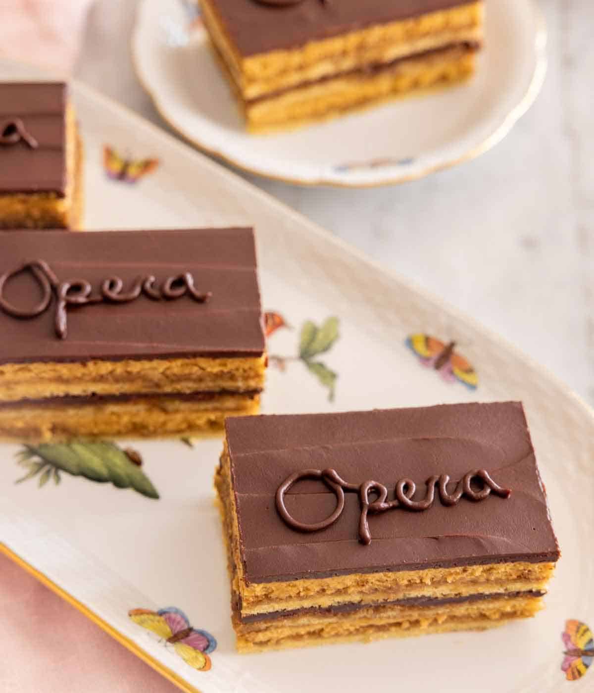A platter with three opera cake pieces with cursive "opera" written on the cake.