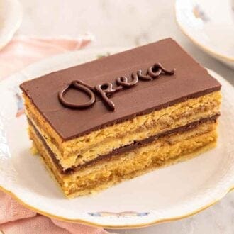 A slice of opera cake with "opera" written on top with a fork beside it.