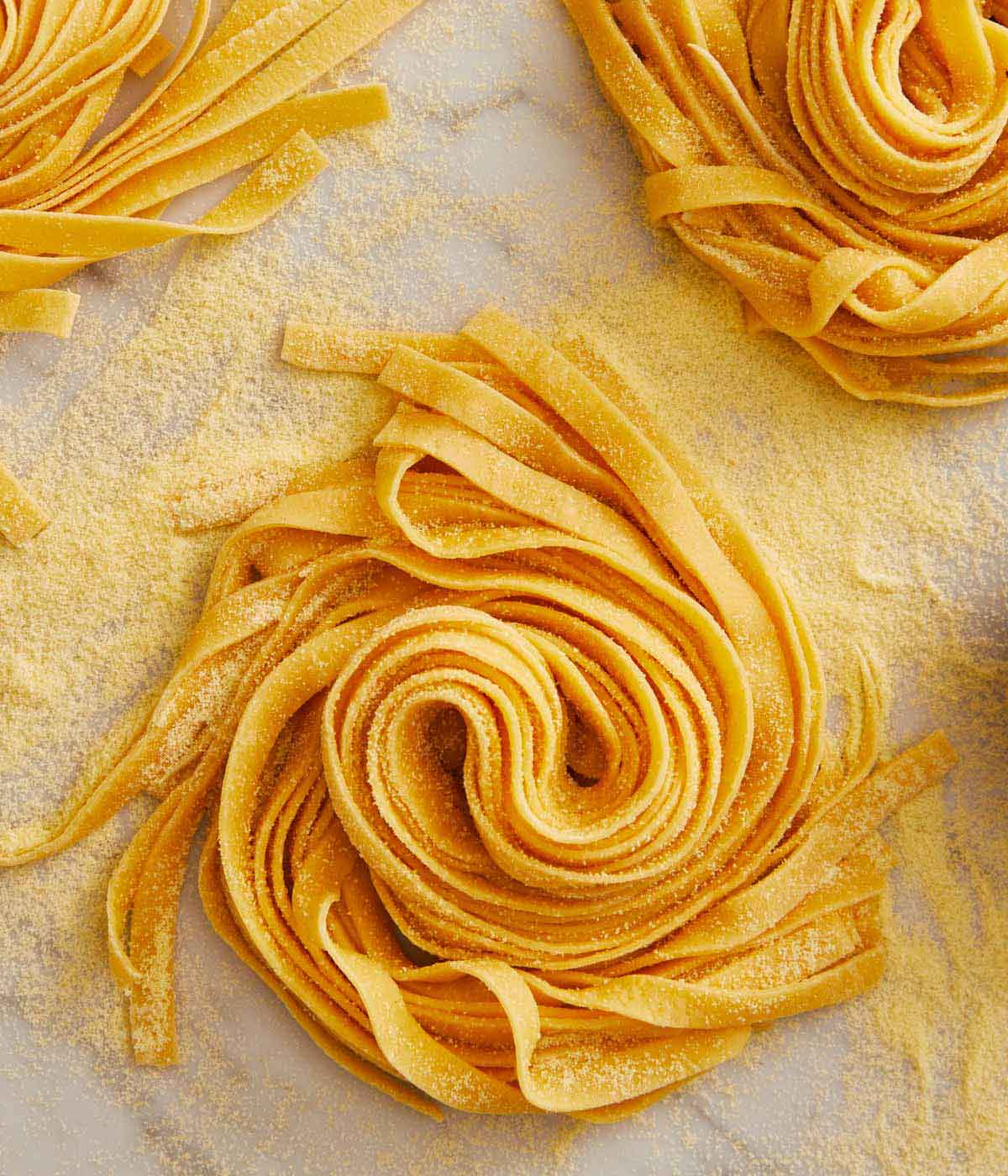 Overhead view of a bundle of long strands of pasta dough with semolina flour sprinkled on top.