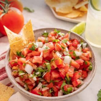 Pinterest graphic of a bowl of pico de gallo with two chips inside of it. More ingredients scattered around the bowl.