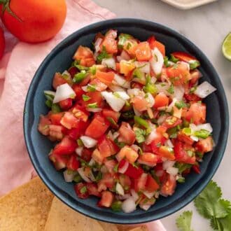 Overhead view of a bowl of pico de gallo with various ingredients scattered around.