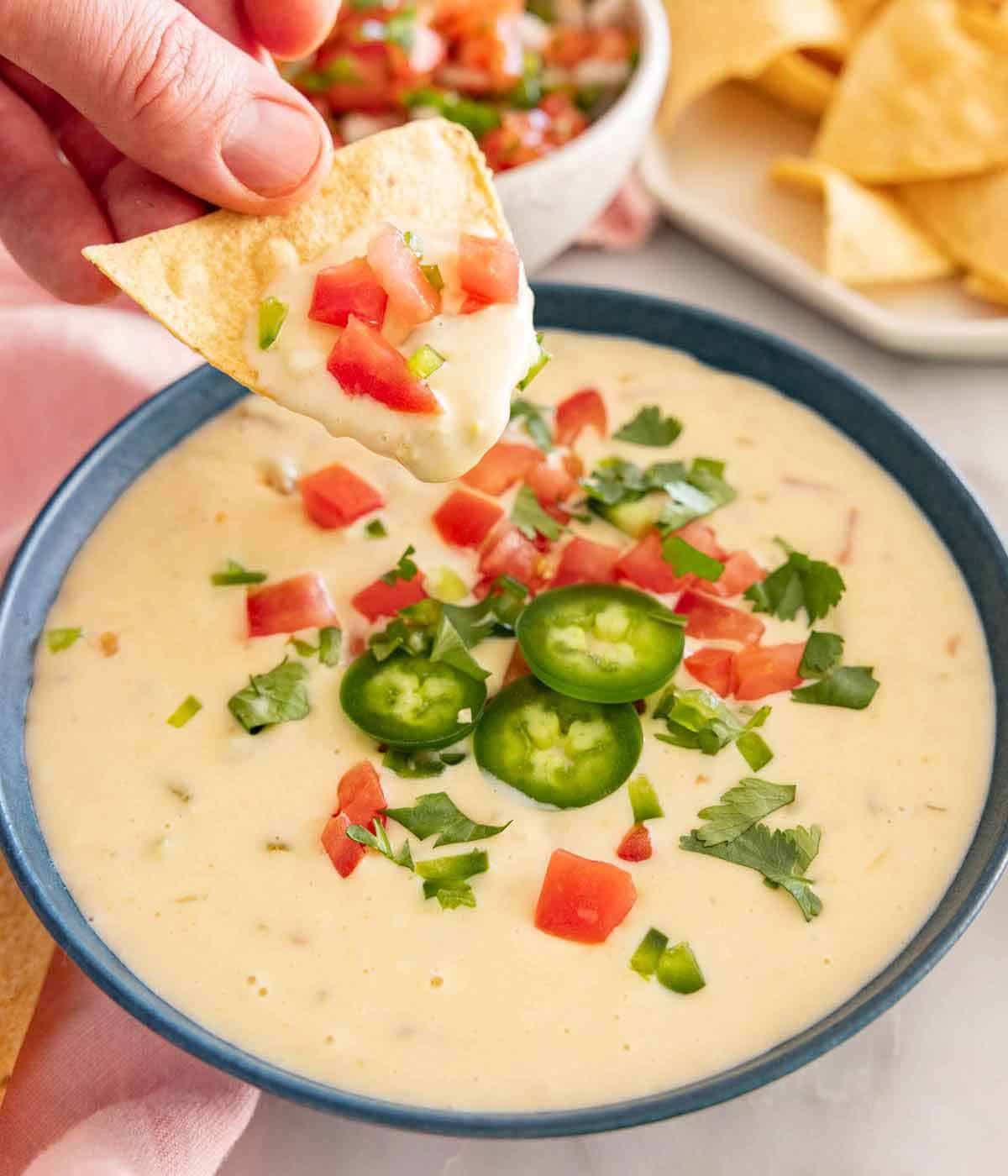 A chip with queso dip on it in front of a bowl of dip.