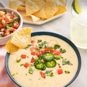 Pinterest graphic of a bowl of queso dip in front of a platter of chips, bowl of pico de gallo, and toppings scattered around.