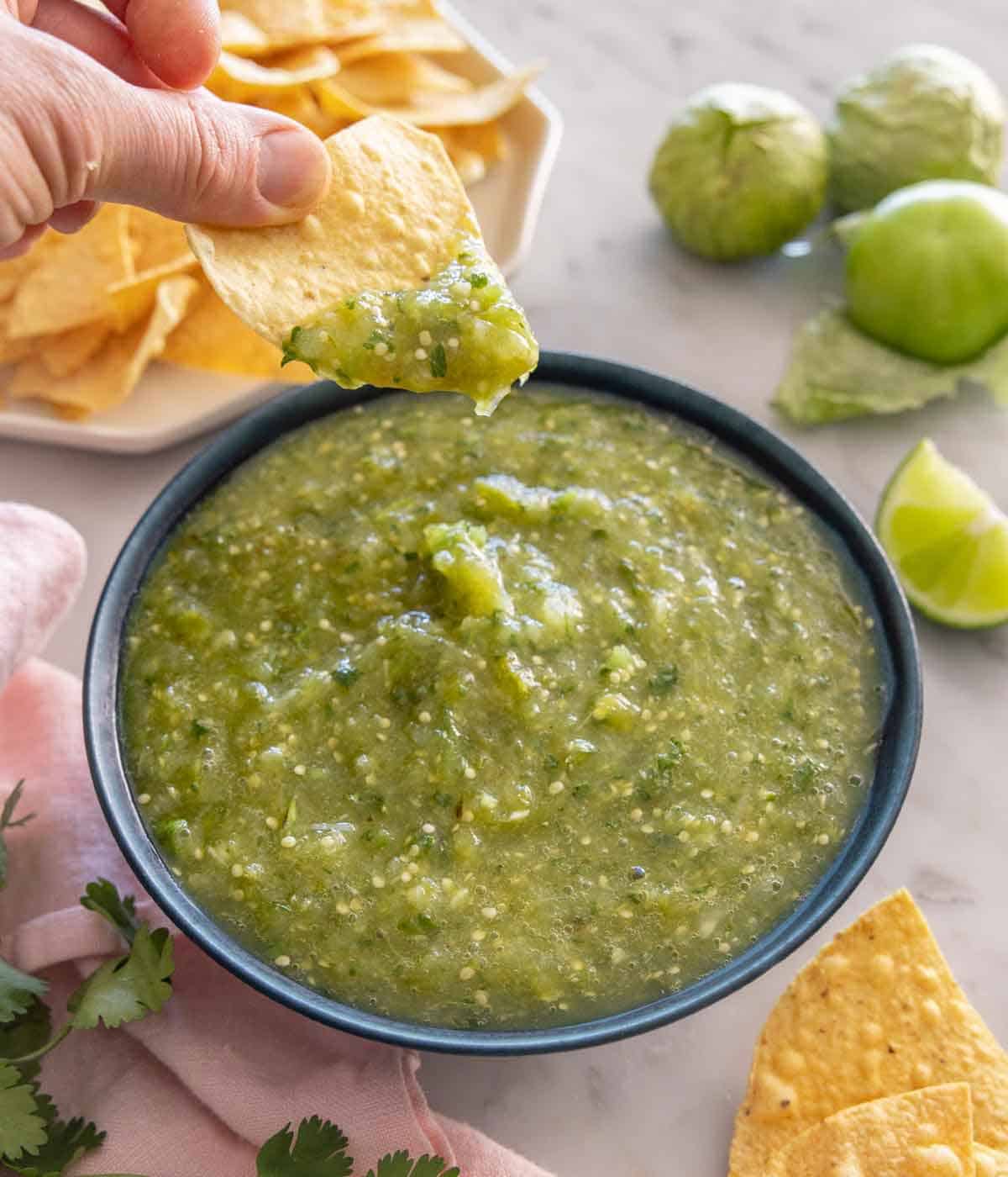 A bowl of salsa verde with tortilla chip scooping some up.