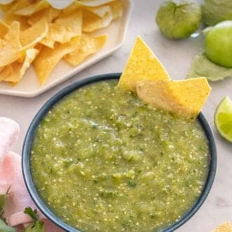 Pinterest graphic of a bowl of salsa verde with two tortilla chips in the bowl with more ingredients by the bowl.