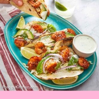 Pinterest graphic of a shrimp taco lifted from a platter with three more with a bowl of dip on the side.