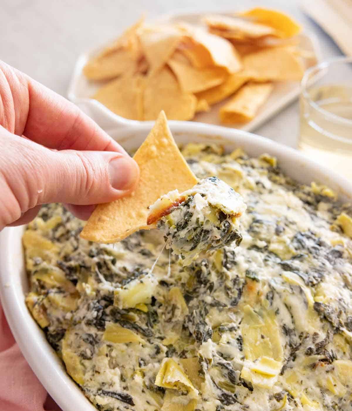 A chip scooping up spinach artichoke dip from a baking dish.
