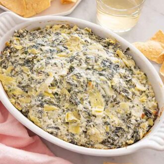 A baking dish with spinach artichoke dip with chips scattered on the side.