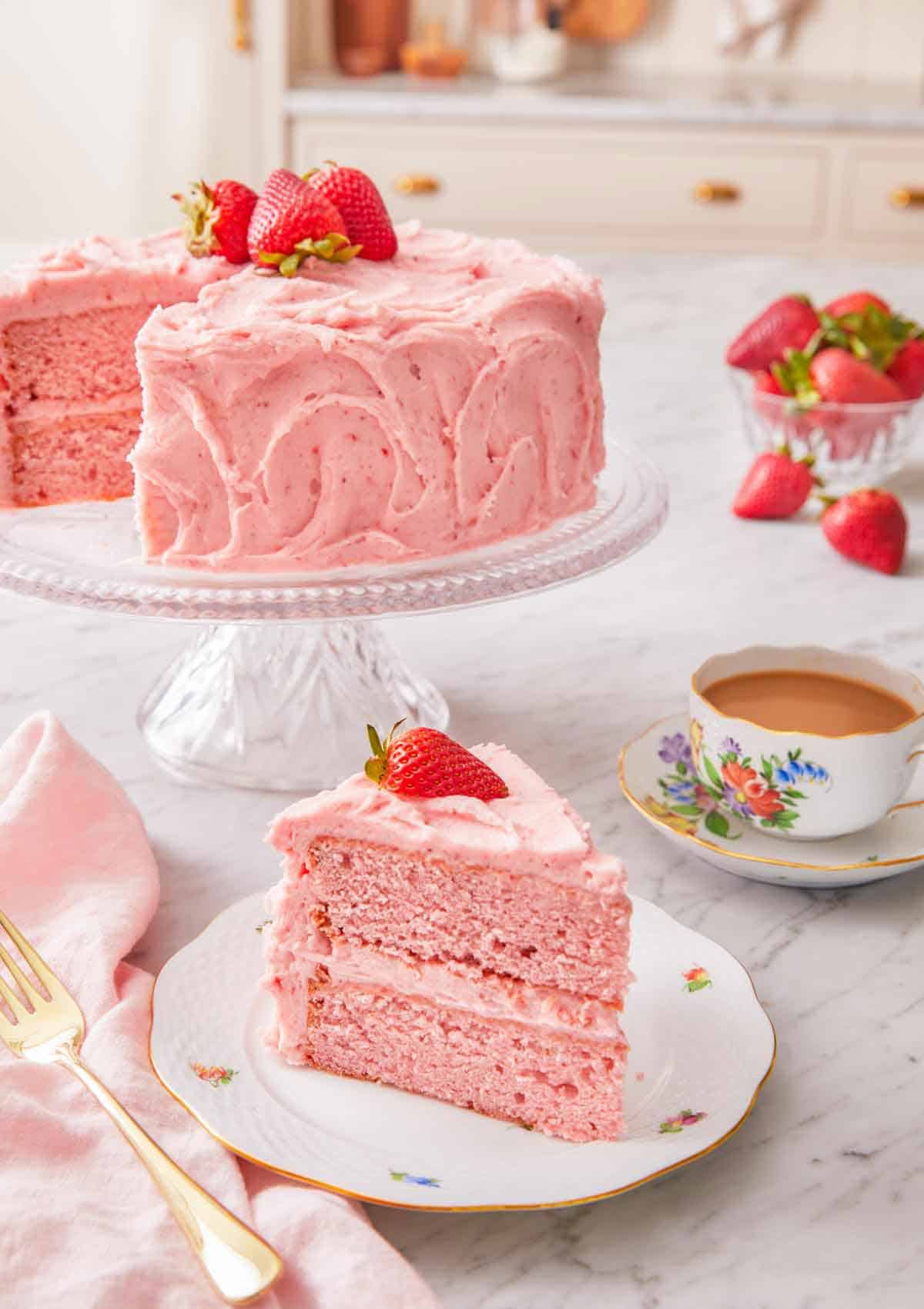 A strawberry cake on a cake stand with a slice cut and placed in front.