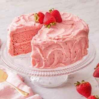 A cake stand with strawberry cake with fresh strawberries on top and in a bowl on the side.