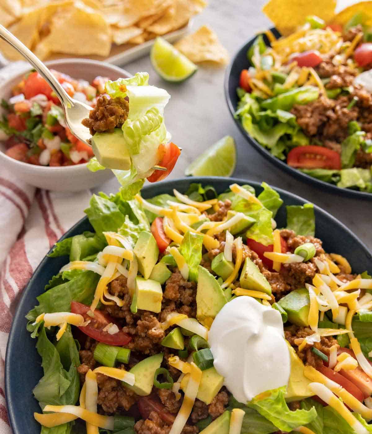 A forkful of taco salad lifted from a bowl with another bowl in the background.
