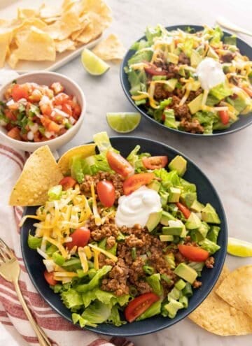 Two bowls of taco salad with a small bowl of pico de gallo and chips on the side.