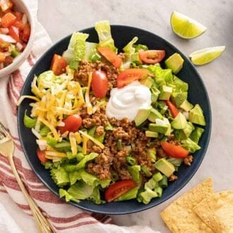 Overhead view of a bowl of taco salad with lime wedges and pico de gallo beside it.