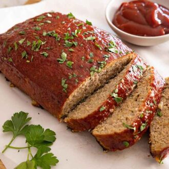 A turkey meatloaf on a lined cutting board with three pieces sliced with a small bowl of sauce in the background.
