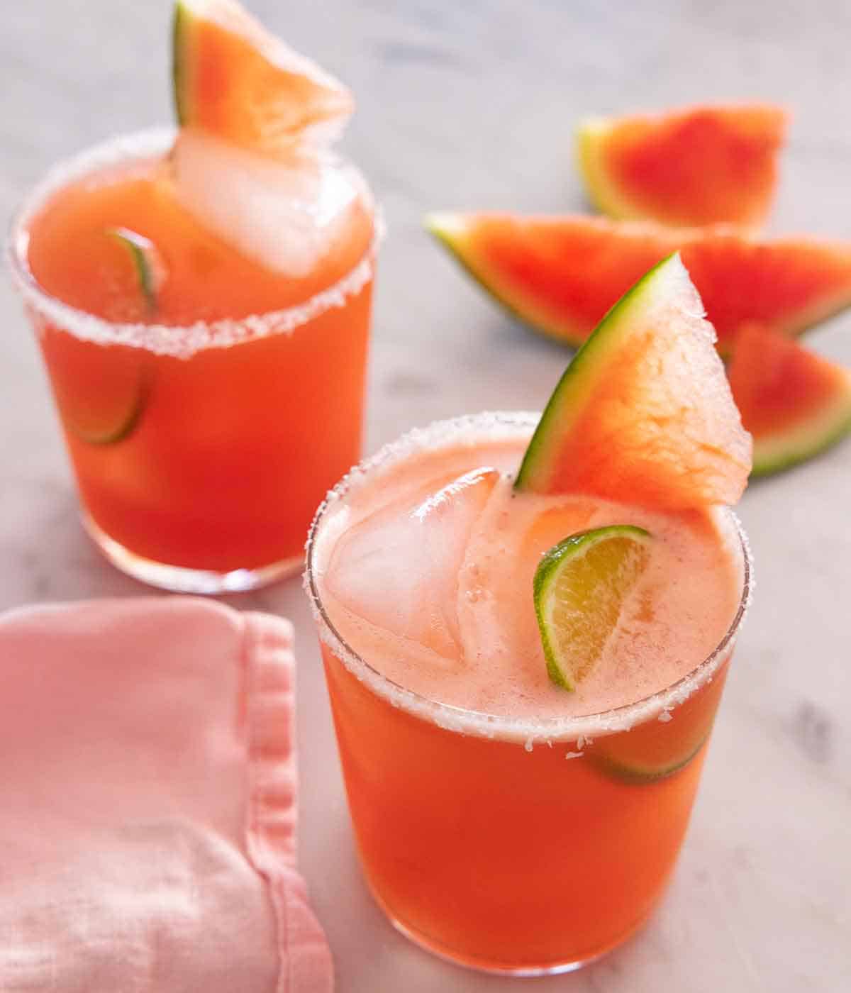 Two glasses of watermelon margaritas with salt on the rim with a slice of watermelon and lime in the drink.