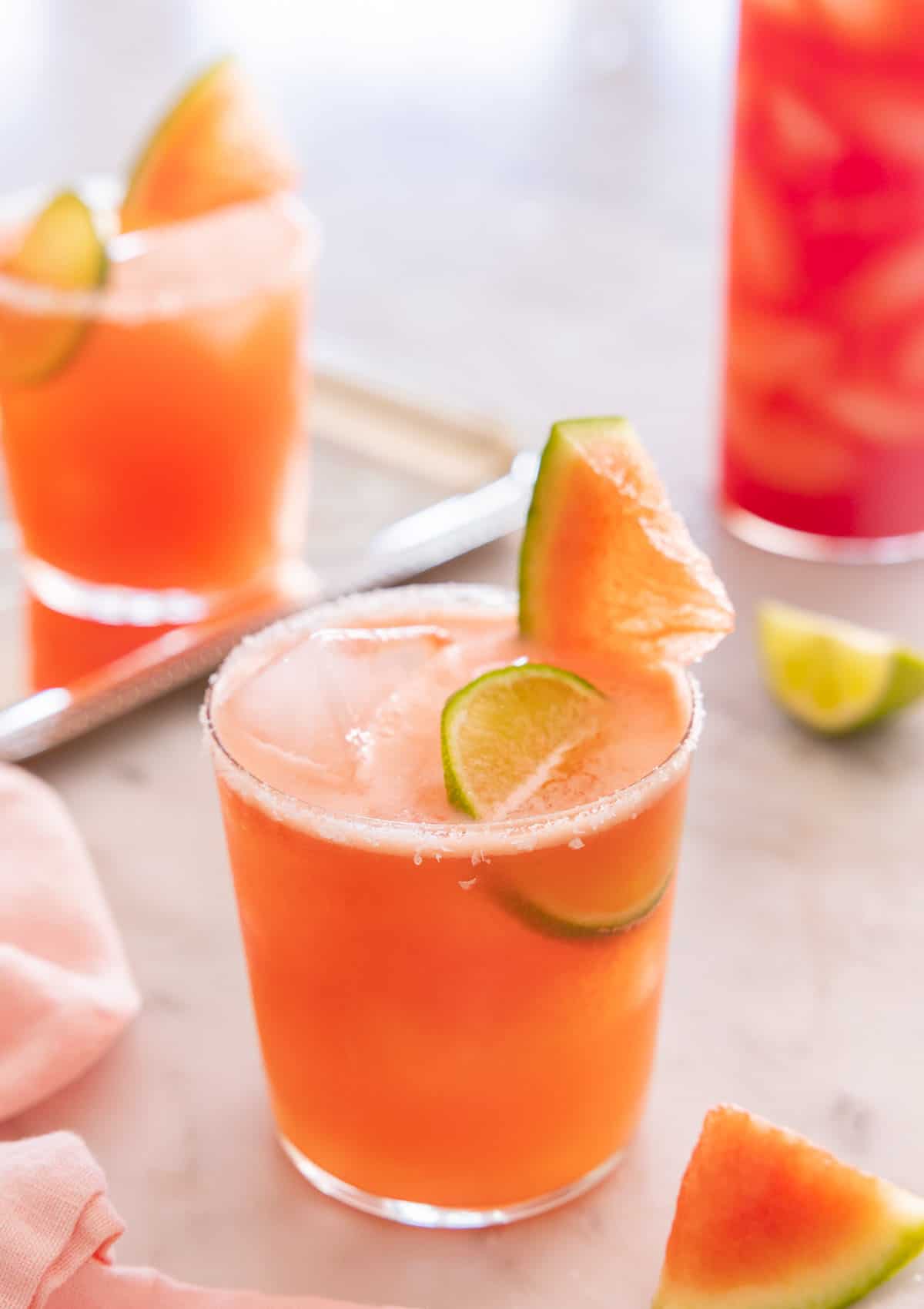 Two short and one tall glass of watermelon margaritas with salt and sliced watermelon on the rim.