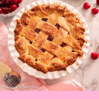Pinterest graphic of an overhead view of a cherry pie in a white pie dish surrounded by fresh cherries scattered and in a bowl.