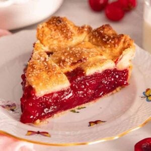 A freshly cut slice of cherry pie on a plate with fresh cherries scattered around.