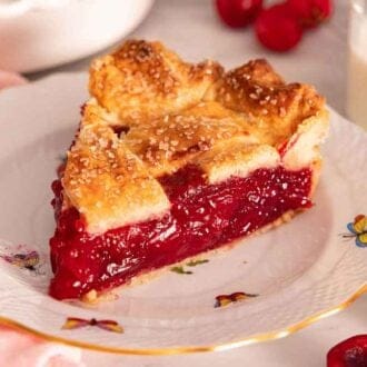 A freshly cut slice of cherry pie on a plate with fresh cherries scattered around.