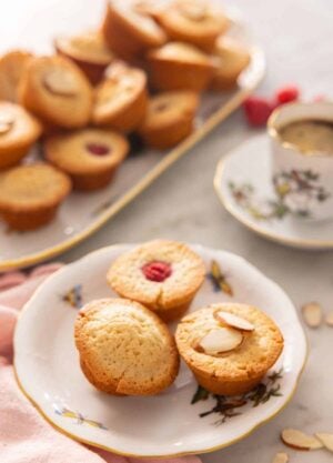 A plate with three financiers on a plate, one plain, one with a raspberry on top, and one with almonds on top.