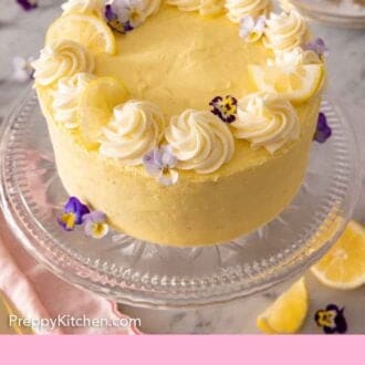 Pinterest graphic of a cake stand with a lemon cake decorated with dollops of frosting, edible flowers, and lemon slices.