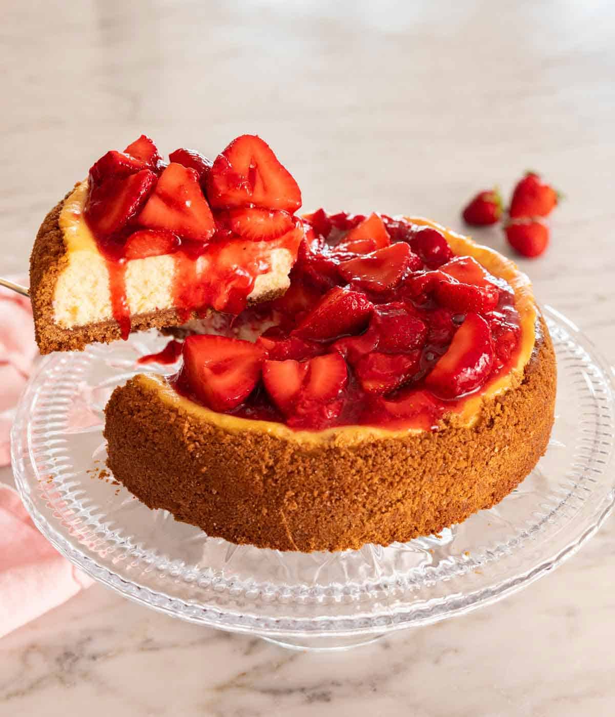 A slice of strawberry cheesecake being lifted from the rest of the cheesecake on a cake stand.