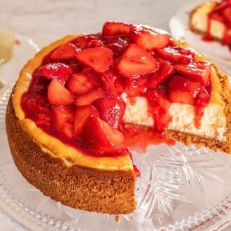 Overhead view of a strawberry cheesecake on a clear cake stand with a quarter cut out.