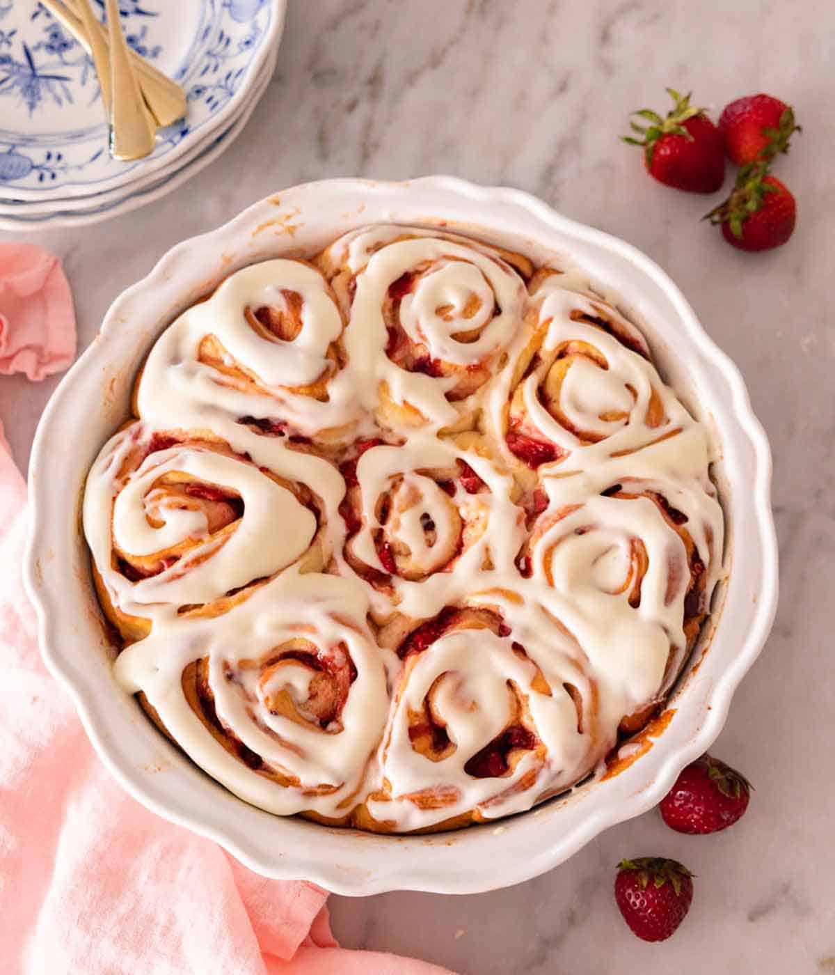 Overhead view of a round baking dish with strawberry rolls with fresh strawberries scattered around.