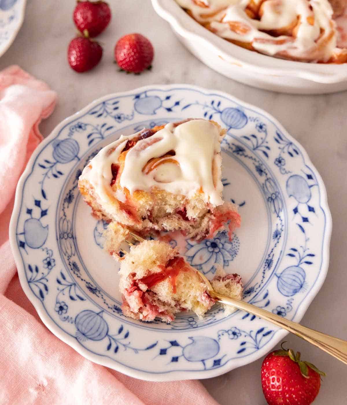 A plate with a piece of strawberry roll with a bite on a fork with fresh strawberries scattered around.