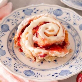 A plate with a strawberry roll with cream cheese icing on top with a fork beside it.