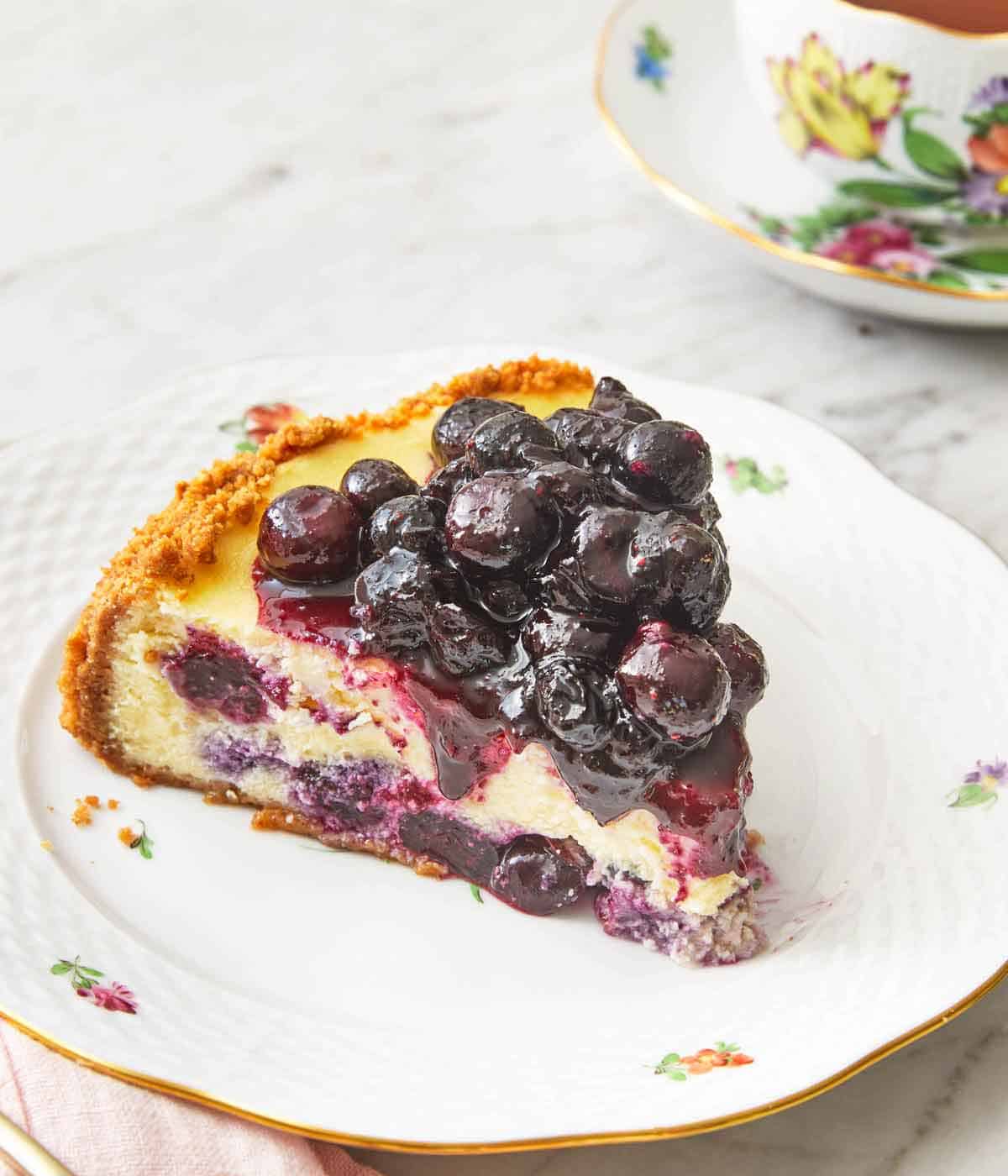 A slice of blueberry cheesecake with blueberry sauce on top, on a plate.