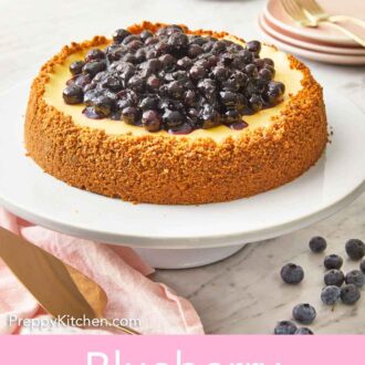 Pinterest graphic of a blueberry cheesecake with a graham cracker crust the goes up the entire side with blueberry sauce on top.