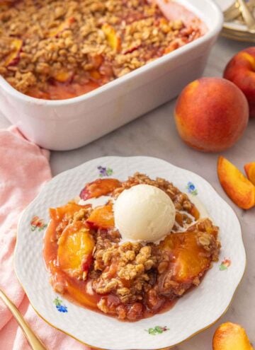 A plate of peach crisp with a scoop of vanilla ice cream on top.
