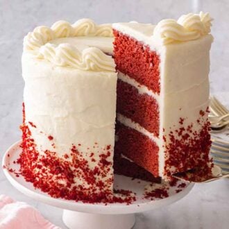 A slice of red velvet cake being lifted from the cake with a stack of plates in the background.