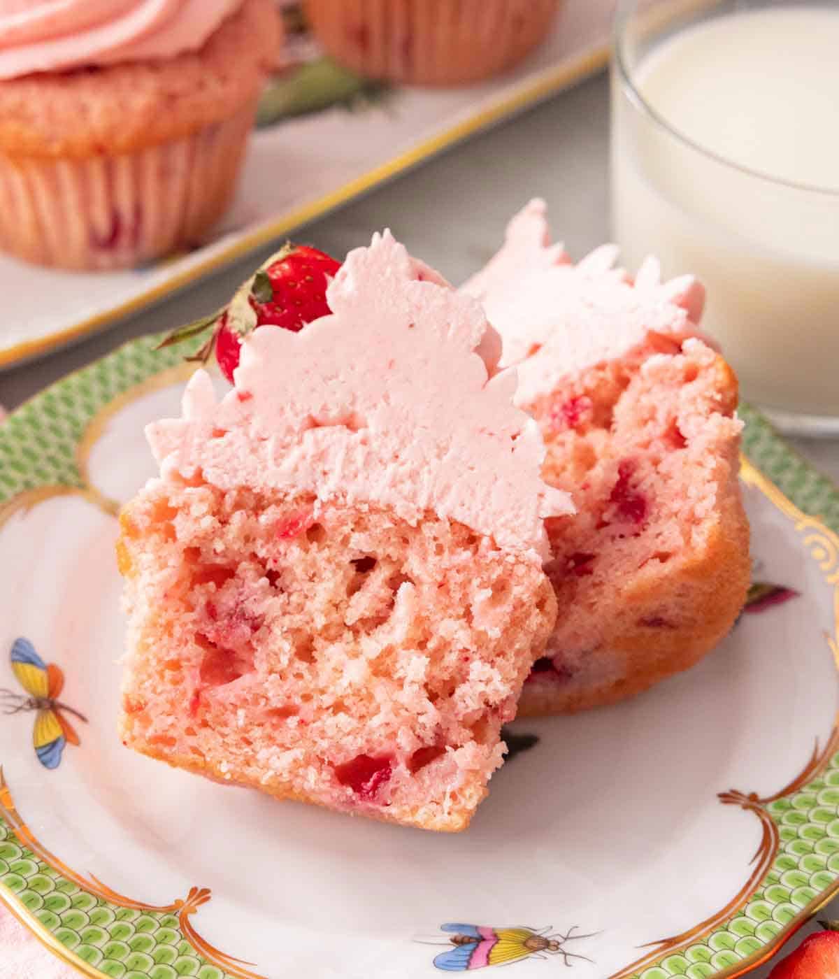 A strawberry cupcake cut in half on a plate.