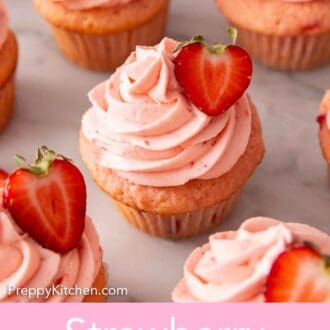 Pinterest graphic of multiple strawberry cupcakes with one in focus in the middle with a cut berry on top of the frosting.