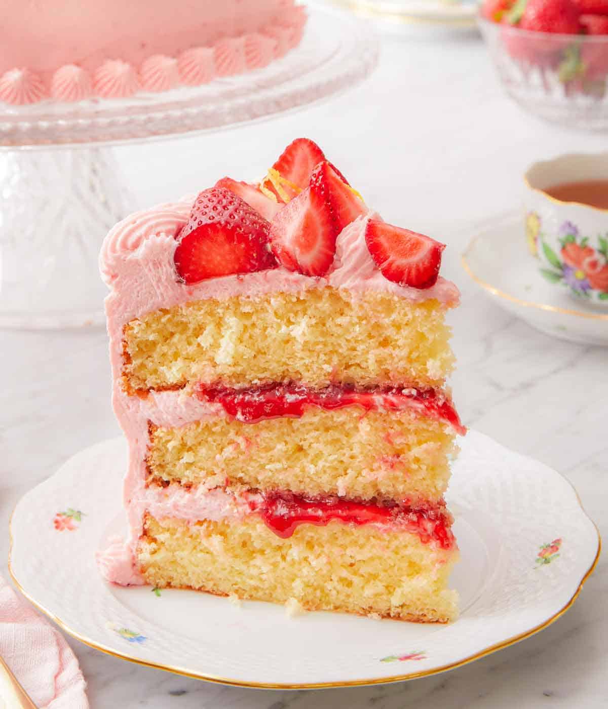 A slice of strawberry lemonade cake showing the three layers with frosting and jam in between the layers.