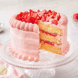 A cake stand with a strawberry lemonade cake with a slice cut on a plate beside it.