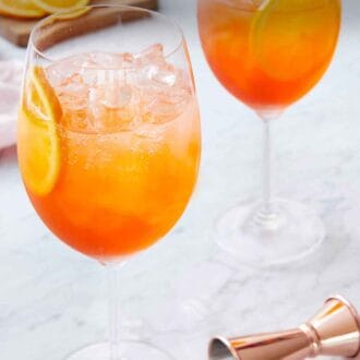 Pinterest graphic of two stemmed wine glasses of aperol spritzes with a jigger in the front.