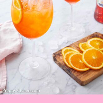 Pinterest graphic of two glasses of aperol spritz with a cutting board with orange slices beside it.