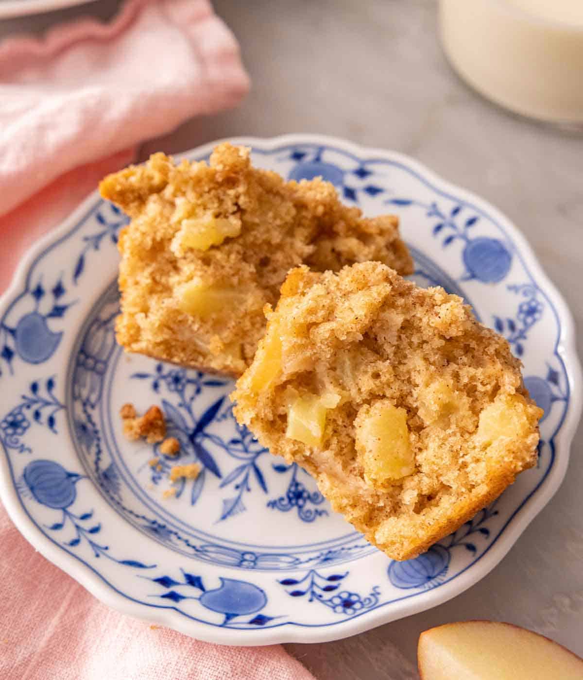 A plate with an apple muffin cut in half, showing the chunks of apples inside the crumb.