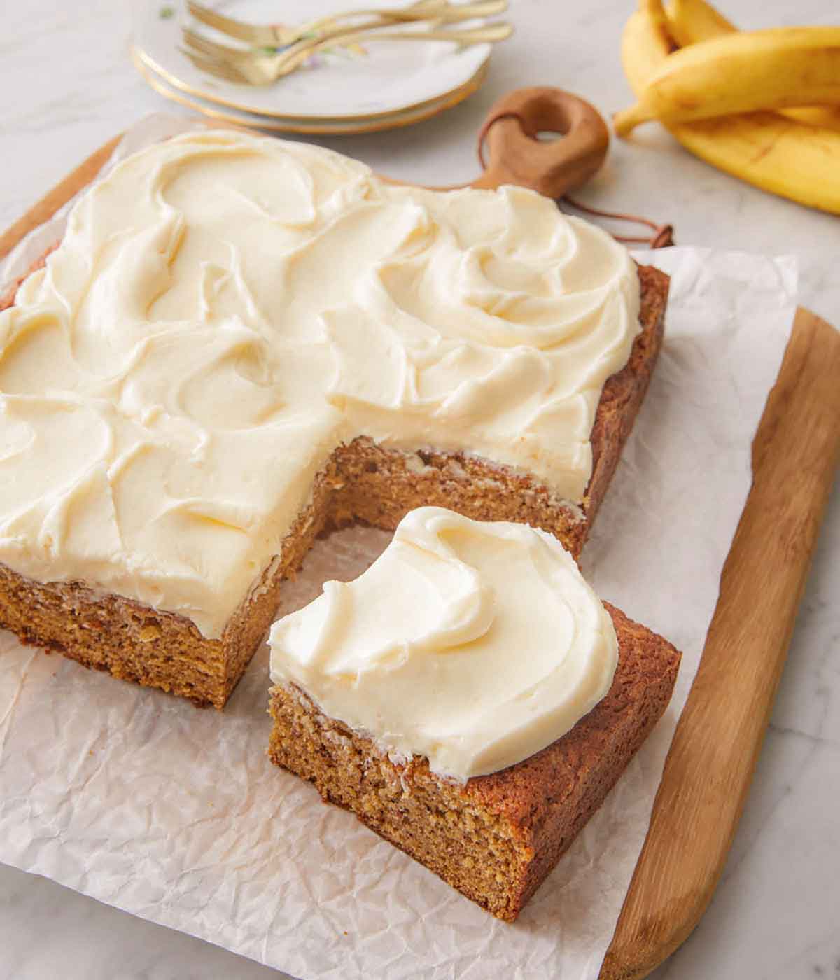 Banana cake on a parchment lined serving board with a serving sliced and pulled forward.